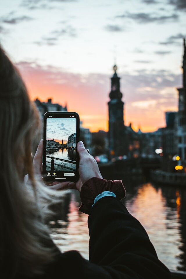 max-van-den-oetelaar-c_Im1a0qmb4-unsplash | Path Social 夕暮れ時にビルの写真を撮る女性。