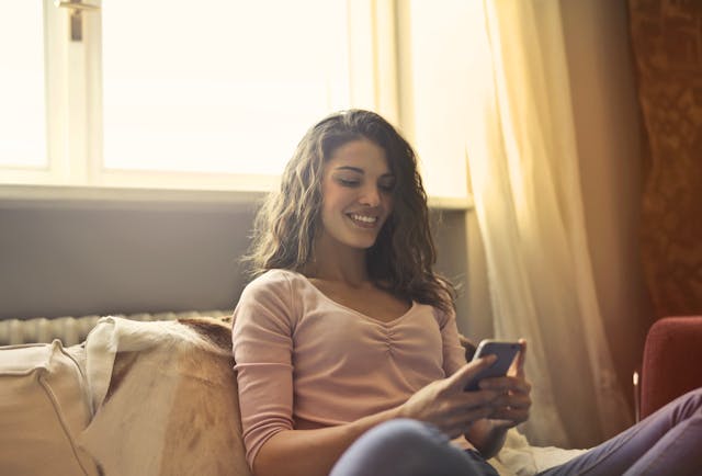 pexels-andrea-piacquadio-3772514 | Path Social A happy woman sitting on the bed while using her phone.
