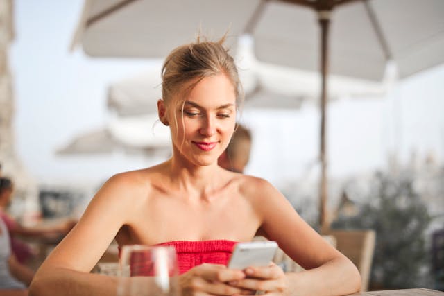 pexels-adrienn-638530-1458437 | Path Social A woman in a red tube top sitting at an outdoor restaurant looking at her smartphone.