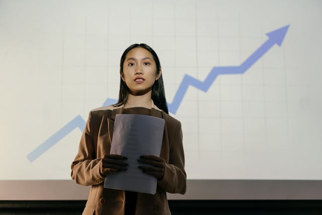 pexels-mikhail-nilov-9304682 | Path Social Une femme en blazer tenant un rapport devant un graphique linéaire montrant la croissance.