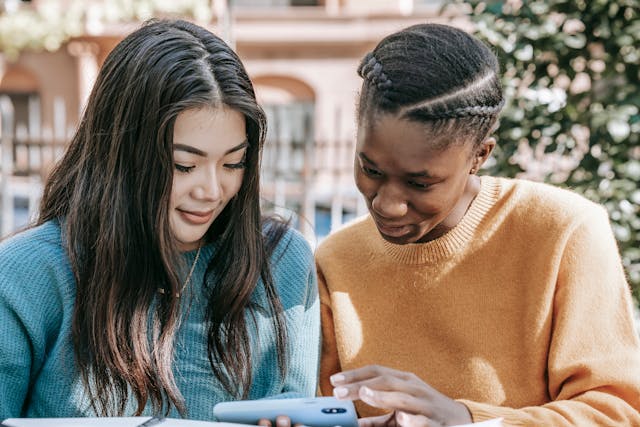 pexels-charlotte-may-5965867 | Path Social Due donne sorridono e guardano insieme un livestream su uno smartphone.