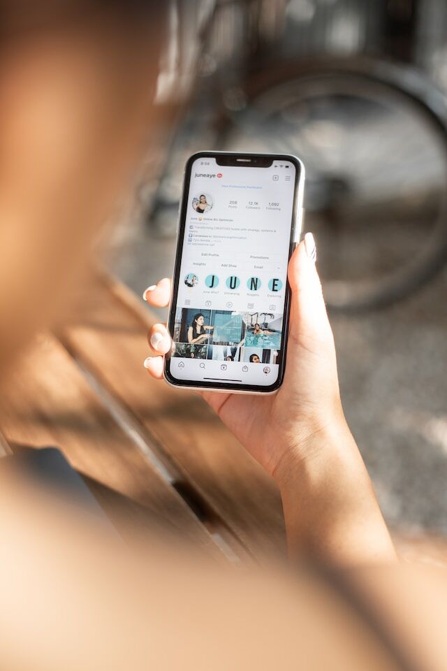 A hand holding a phone, looking at an Instagram account.