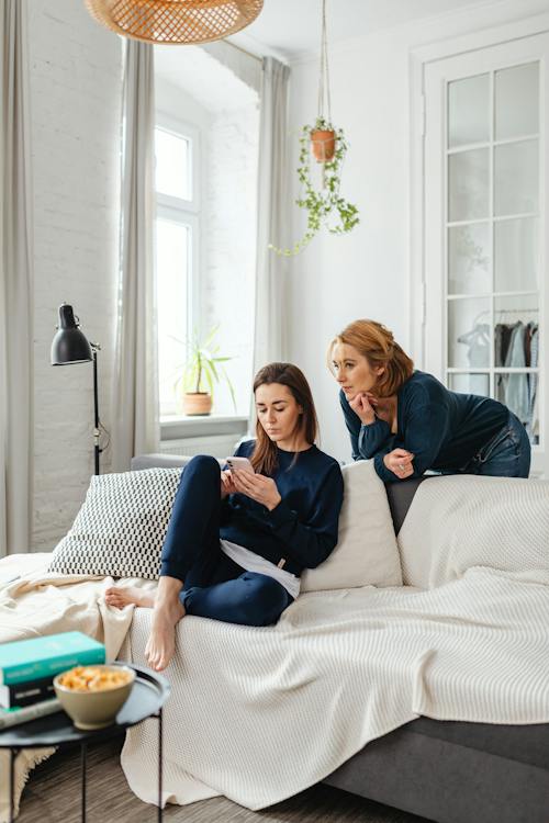 Two women looking at a mobile phone, one sitting, one standing.