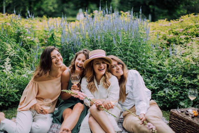 A group of female friends laughing and leaning on each other while having a picnic in a garden.