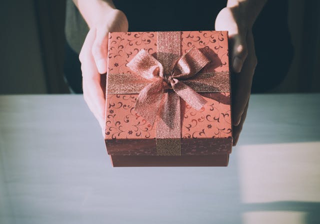 Someone holding a brown gift box tied with a sparkly ribbon.