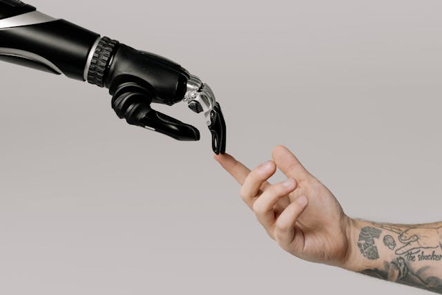 A man’s index finger pointing upward to touch a robotic hand’s fingertips.