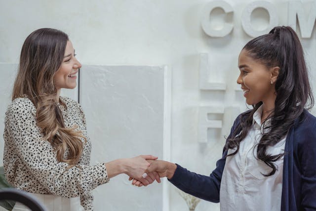 Deux jeunes femmes se sourient et se serrent la main dans un bureau.