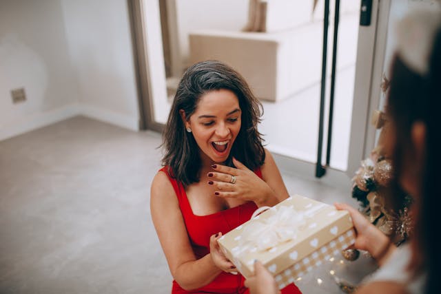 A woman in a red dress with a surprised face after receiving a gift from someone.