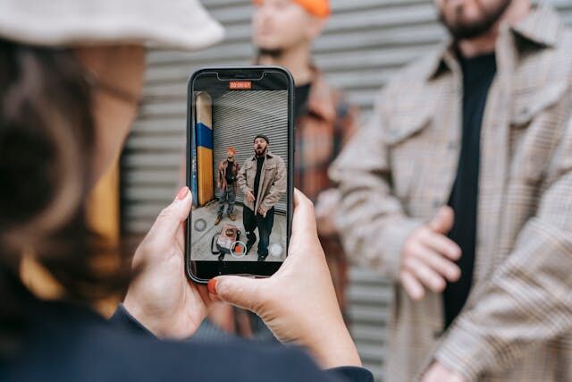 Someone holding a smartphone to record a video of two guys in front of a garage door.