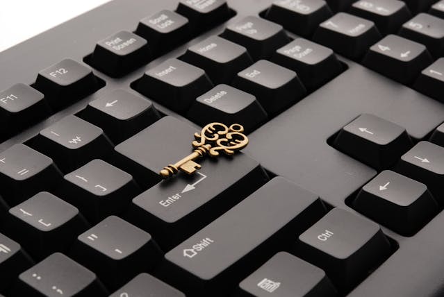 A black computer keyboard with an ornate golden key on top of it.