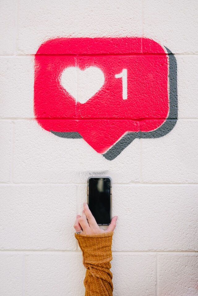위에 빨간색 말풍선이 있는 전화기를 들고 있는 손, 하트와 해시태그를 나타내는 숫자 1 Instagram 좋아요를 얻기.