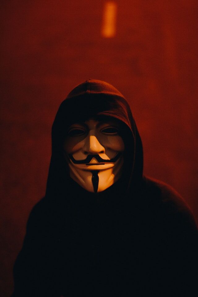 Dark figure in a black hoodie and face mask.