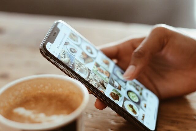Path Social prim-plan al unei mâini care parcurge o grilă de profil Instagram lângă o ceașcă de cafea.