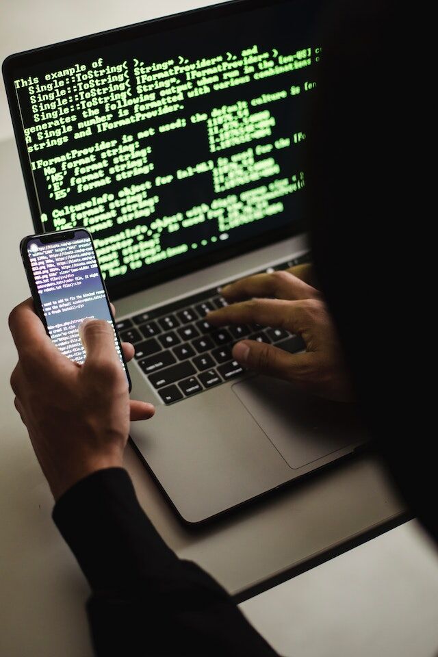 Un hacker anonim codifică pe un telefon și un laptop.
