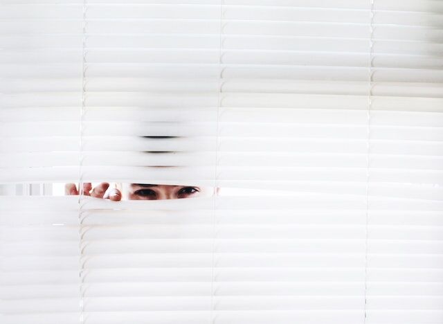 O persoană care trage cu ochiul pe ascuns prin jaluzelele ferestrelor.