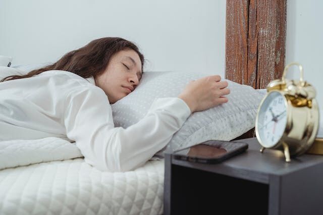 一個女人以舒適的面朝下姿勢睡在床上，同時忽略了她的鬧鐘。