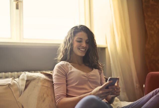 ベッドに座って携帯電話を使う幸せそうな女性。